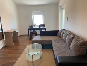 Un salon comprenant une table basse en verre, un canapé, une table à manger avec des chaises et une fenêtre.