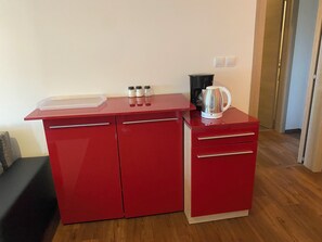Une petite cuisine de couleur rouge, équipée d’une machine à café, d’une bouilloire et d’un petit plan de travail.
