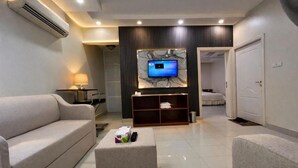 Una sala moderna con sofá, una mesa de centro, un televisor de pantalla plana montado en la pared y una puerta que da a otra habitación.