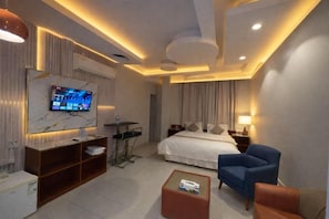 A modern hotel room with a bed, a desk, a TV, and a seating area.