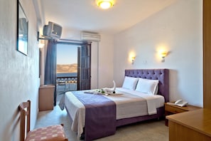 A hotel room with a bed, a desk, a chair, a TV, and a balcony with a view.