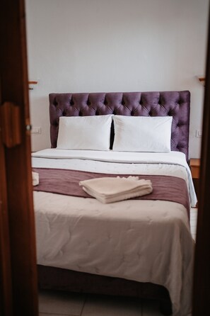 Una cama con cabecera capitonada, ropa de cama blanca y marrón, y una manta blanca doblada sobre la cama.