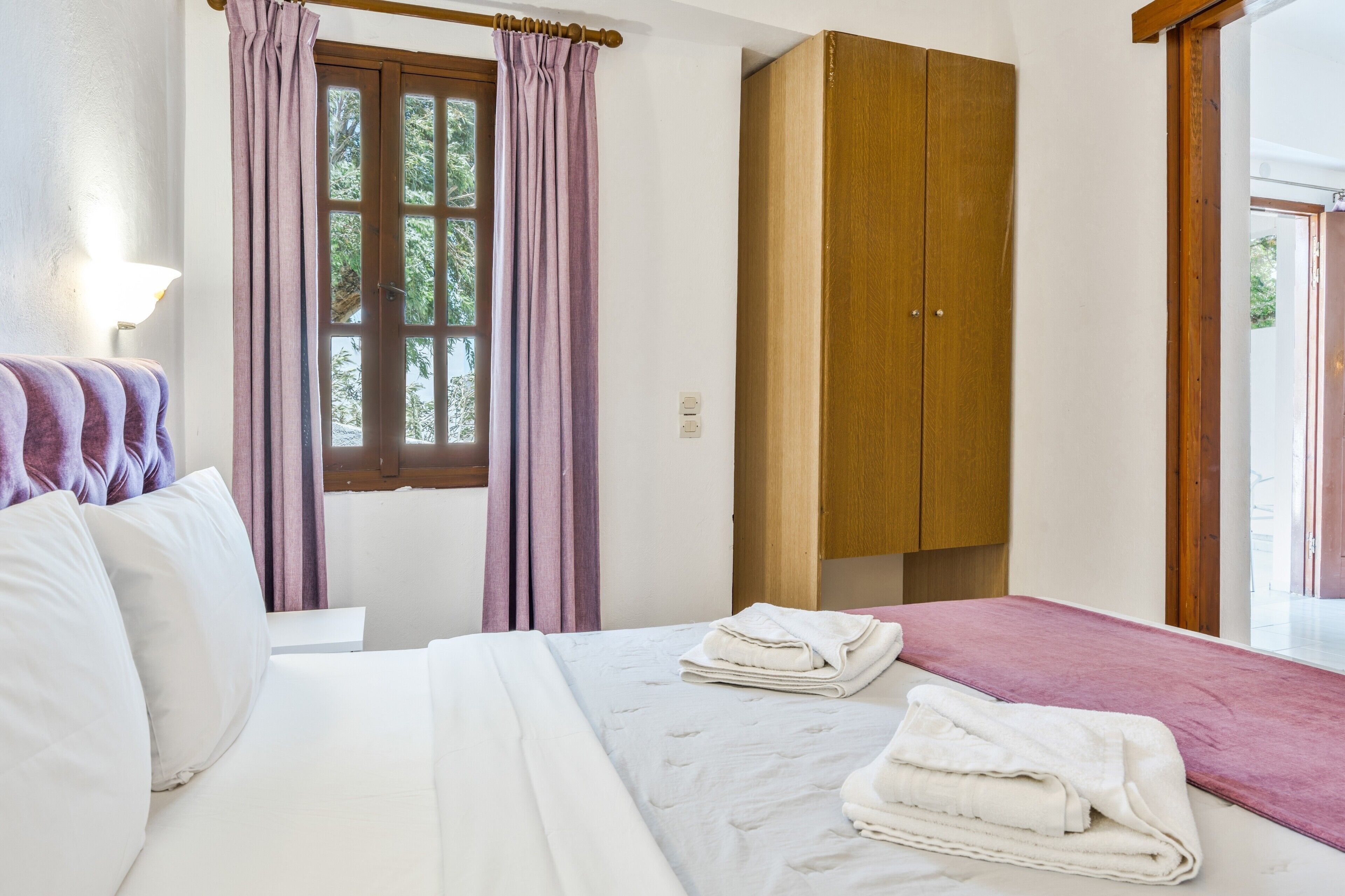 Une chambre d’hôtel avec un lit, une armoire, une fenêtre avec des rideaux et une vue sur la verdure.