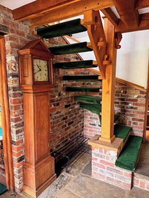 A wooden grandfather clock, a brick wall, and a wooden staircase with green carpet steps.