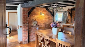 Een landelijke eethoek met een bakstenen muur, houten balken in het plafond en een houten tafel met stoelen.