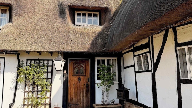 Een landelijke cottage met rieten dak, een houten deur, een klein raam en een grindpad naar de ingang.