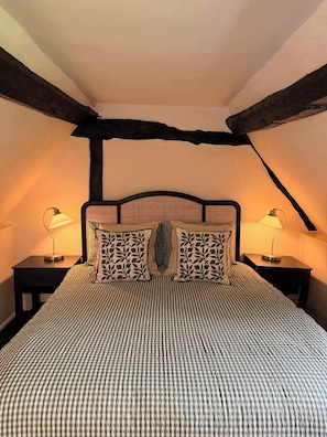 A bedroom with a checkered bedspread, two bedside lamps, and a headboard with a leaf pattern. - Mesopotamia Cottage Country Hideaway (Clifton Hampden)