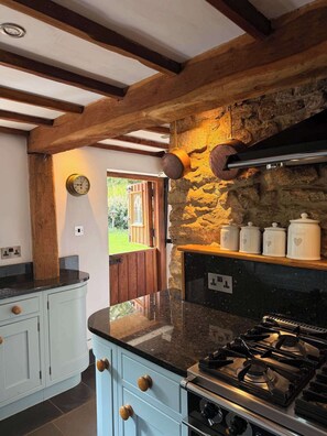 A kitchen with a stone wall, a stove, and a clock.