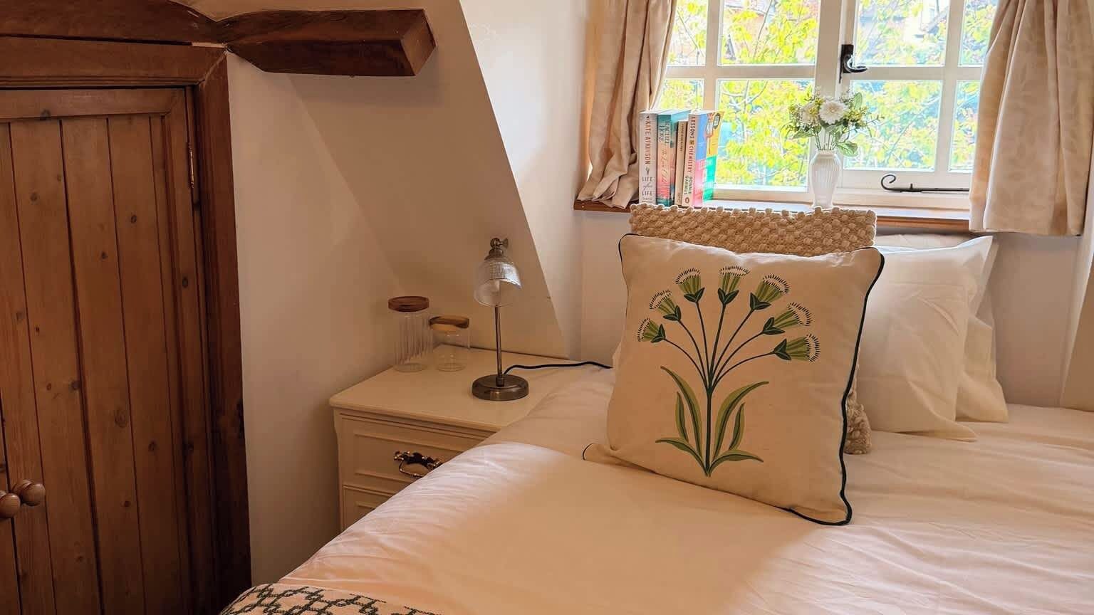 Un dormitorio con cama, mesita de noche, lámpara, ventana con cortinas y puerta de madera.