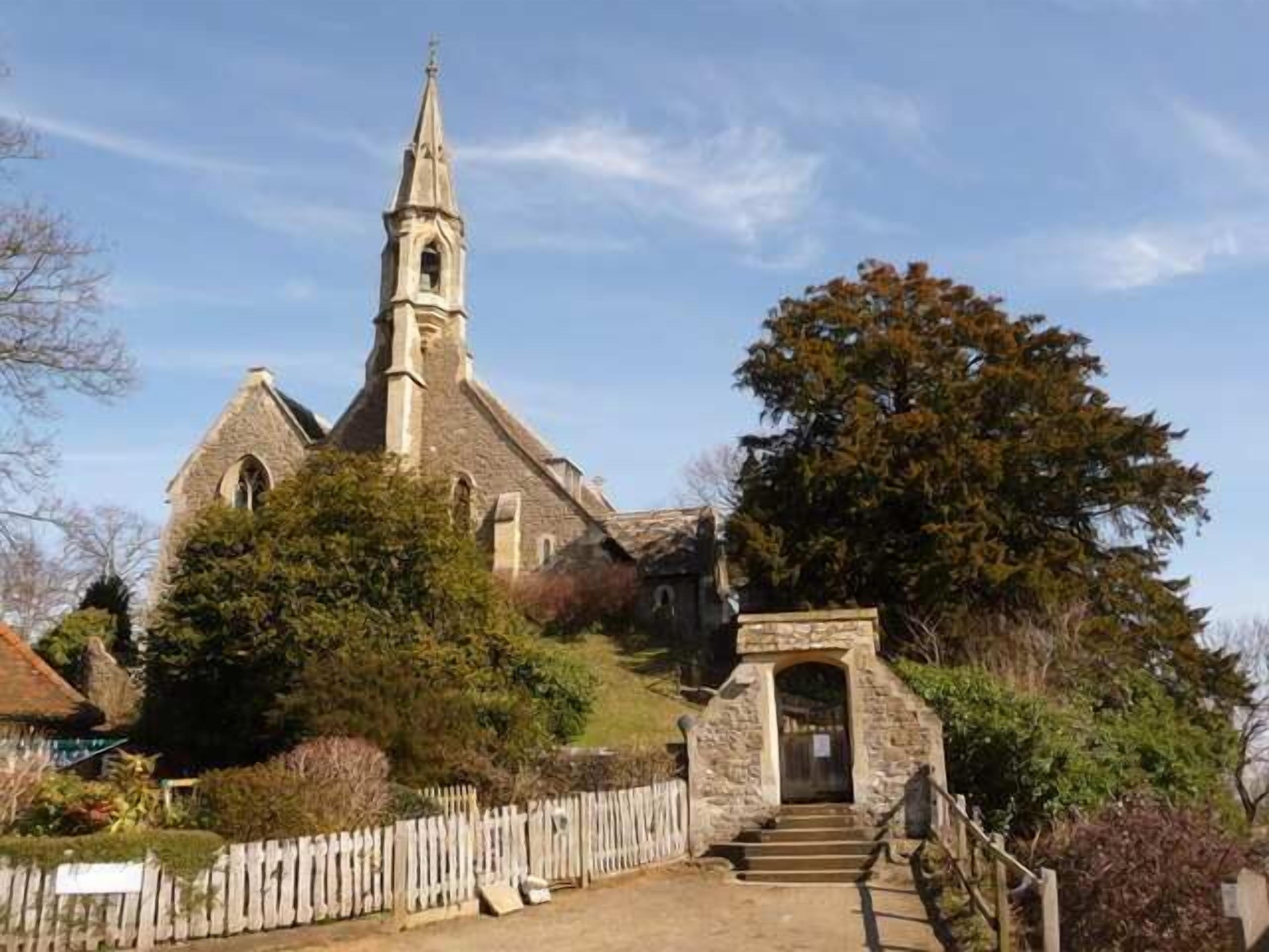 A church with a prominent steeple, a stone entrance, and a wooden fence in the foreground.