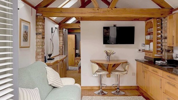 Une pièce de style loft avec un plafond en pente, un coin repas avec deux tabourets de bar, un canapé et une petite table sur laquelle est posé un vase.
