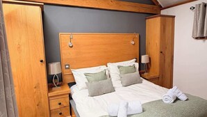 Une chambre à coucher avec une tête de lit en bois, un lit avec une literie blanche, une table de chevet, une armoire et un puits de lumière.