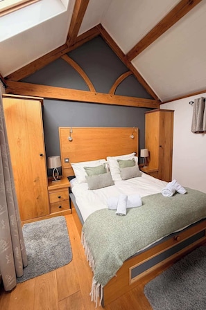 A bedroom with a wooden headboard, a bed with white bedding, a nightstand, a wardrobe, and a skylight.