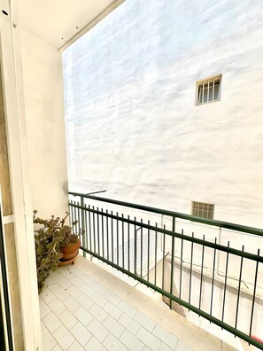 A balcony with a potted plant, a metal railing, and a building with a window in the background. - 'Art Vintage-French Double' Room with Balcony, Wi-Fi & Air Conditioning (Noicàttaro)