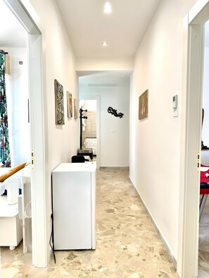 A hallway with a white desk, artwork on the walls, and a tiled floor. - 'Art Vintage-French Double' Room with Balcony, Wi-Fi & Air Conditioning (Noicàttaro)