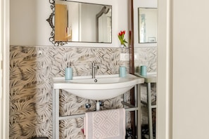 Ein Badezimmer mit einem weißen Waschbecken, zwei blauen Seifenspendern, einem Spiegel mit dekorativem Rahmen und einer Wand mit einem blattmusternden Fliesendesign.