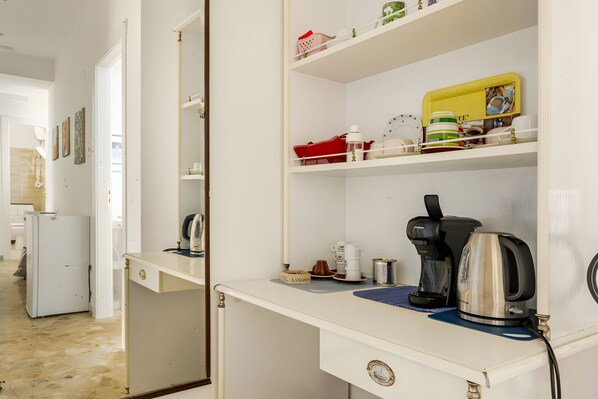 Un bureau blanc avec une machine à café, une bouilloire et une petite étagère contenant divers objets.