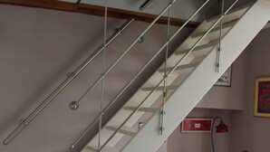Eine Treppe mit Metallgeländern, ein Holztisch, ein Stuhl mit Kissen sowie ein Schrank.