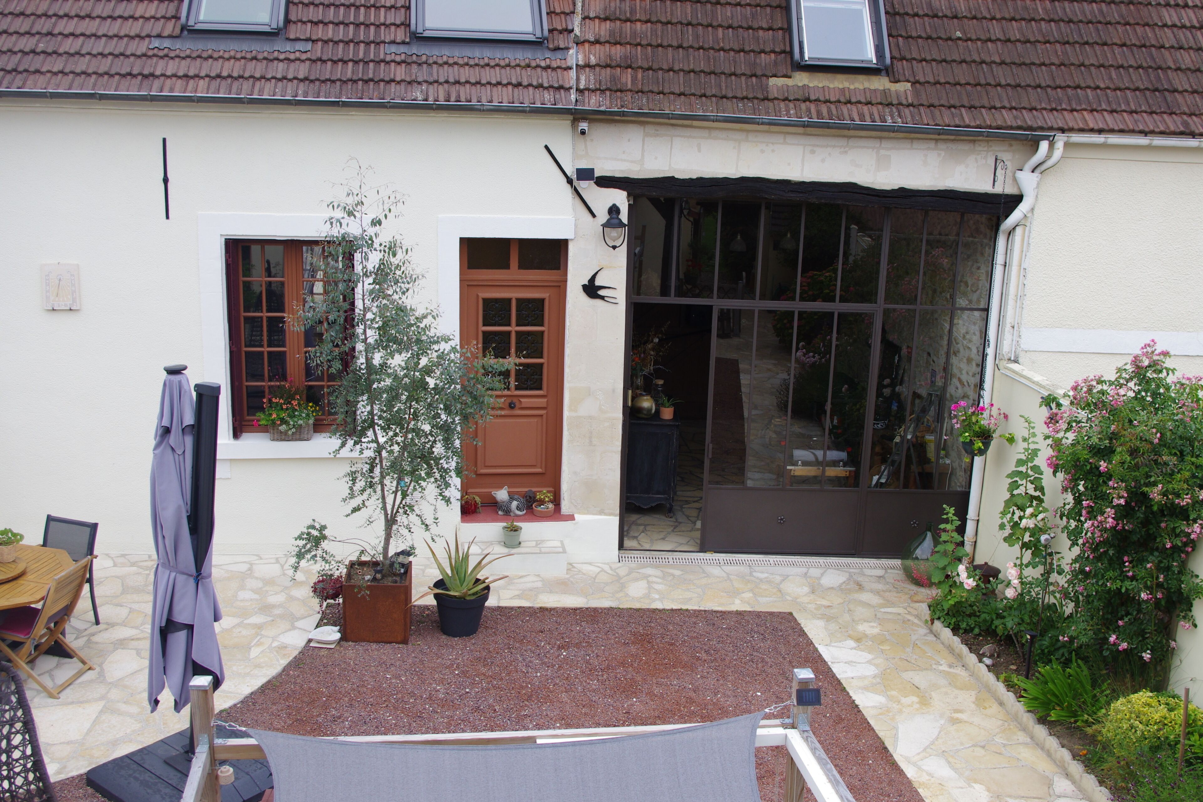 A house with a stone patio, a wooden table, a potted plant, and a door with glass panels.