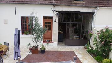 A house with a stone patio, a wooden table, a potted plant, and a door with glass panels.