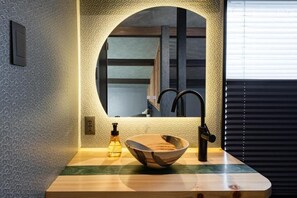 Une salle de bain avec un meuble-lavabo en bois, un miroir rond, un robinet noir et un flacon de savon.