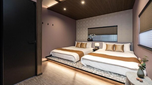 A hotel room with two beds, a wooden ceiling, a small table with a vase, and a window with blinds. - JAPAVISTA Hinata (KONOHANA WARD)
