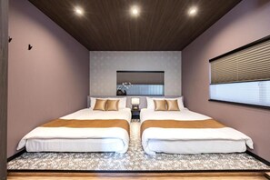 Une chambre d’hôtel avec deux lits, un plafond en bois, une grande fenêtre avec des stores et un miroir au-dessus des lits.