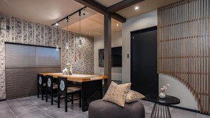 A modern interior with a wooden dining table, chairs, a black sofa, and a small round table with a vase. - JAPAVISTA Hinata (KONOHANA WARD)