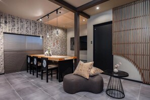 A modern interior with a wooden dining table, chairs, a black sofa, and a small round table with a vase. - JAPAVISTA Hinata (KONOHANA WARD)