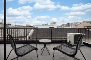 A balcony with two chairs and a small table, overlooking a cityscape with buildings and a clear sky. - JAPAVISTA Hinata (KONOHANA WARD)