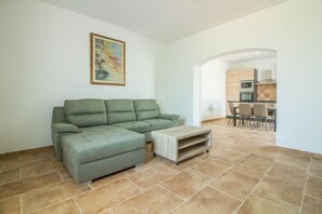 A living room with a sectional sofa, a coffee table, and a painting on the wall. - GuestHost - Lovely Apartment by the Vineyard (Arzachena)