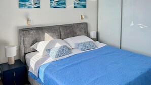 Ein Bett mit blauer Bettdecke, zwei Kissen, einem grauen Kopfteil und Wandbildern mit Segelbooten.