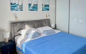 A bed with a blue bedspread, two pillows, a grey headboard, and wall art depicting sailboats. - 2 bedroom cozy apartment in Sibenik (Sibenik)