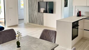 Eine moderne Küche mit Einbauofen, ein Essbereich mit Tisch und Stühlen sowie ein an der Wand montierter Fernseher.
