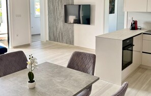 Eine moderne Küche mit Einbauofen, ein Essbereich mit Tisch und Stühlen sowie ein an der Wand montierter Fernseher.