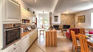Une cuisine moderne dotée d’appareils électroménagers intégrés, un coin repas avec un canapé à carreaux rouges et une cheminée en pierre.