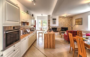 Eine moderne Küche mit integrierten Geräten, eine Essecke mit einem rot karierten Sofa und ein Kamin aus Stein.