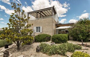 Ein modernes Haus mit Steinverkleidung, einer überdachten Terrasse und einem gepflegten Garten.