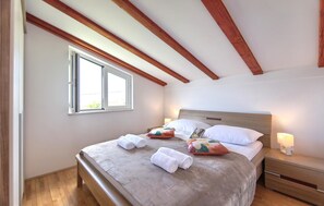 Ein Schlafzimmer mit Bett, Holzbalken, einem Fenster und einem Nachttisch mit Lampe.