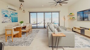 A modern living room with a sofa, dining table, chairs, a ceiling fan, and a large window. - Casa Luna  By FMI Rentals (Puerto Peñasco)