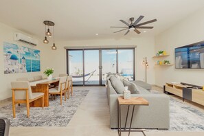 Ein modernes Wohnzimmer mit einer Couch, einem Esstisch, Stühlen, einem Deckenventilator und einem großen Fenster.