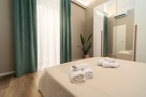 A hotel room with a bed, a potted plant, a mirror, and a door. - Archimede Suites (Catania)