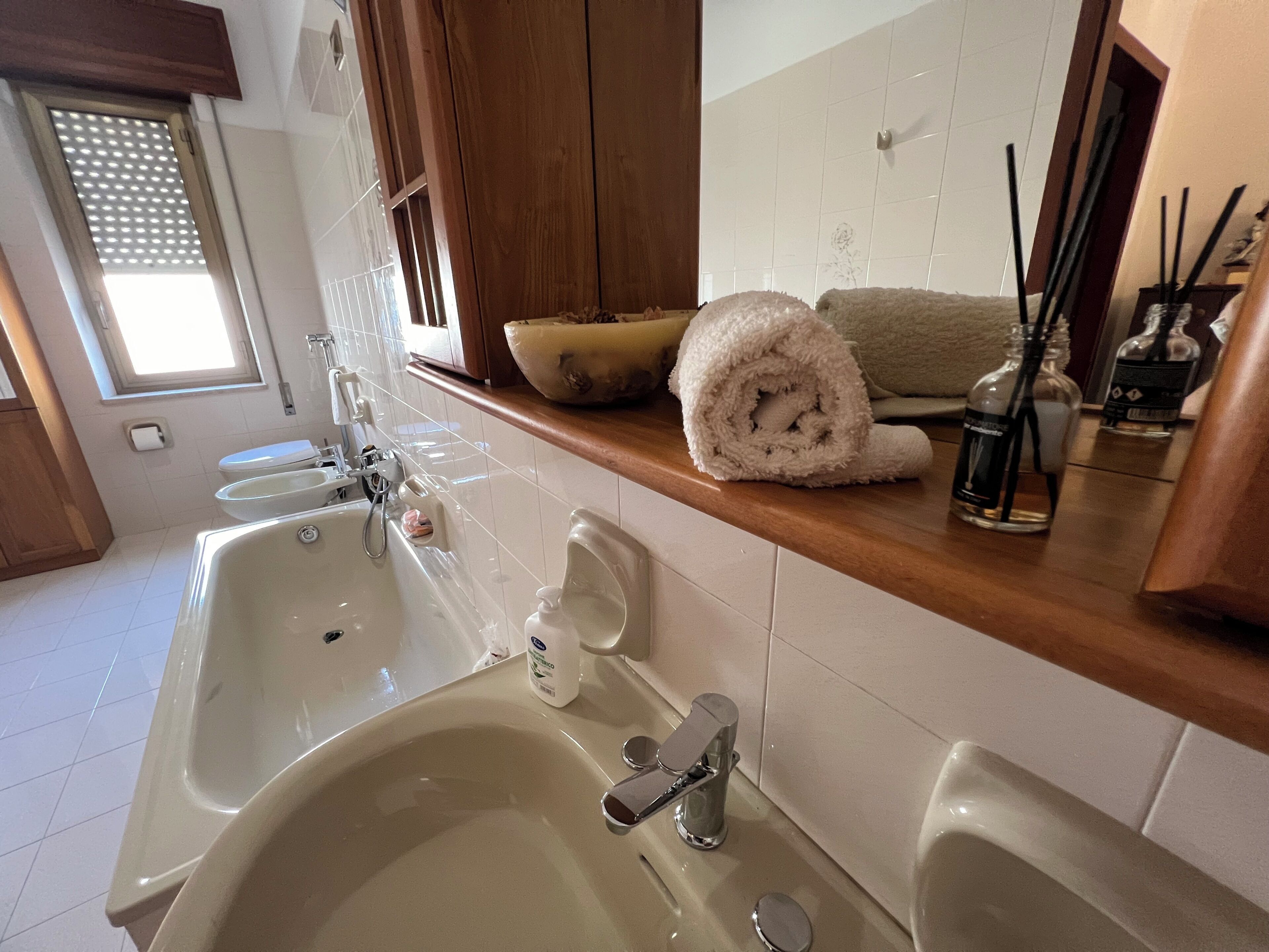 Un baño con dos lavamanos, un espejo, un perchero para toallas y una ventana.