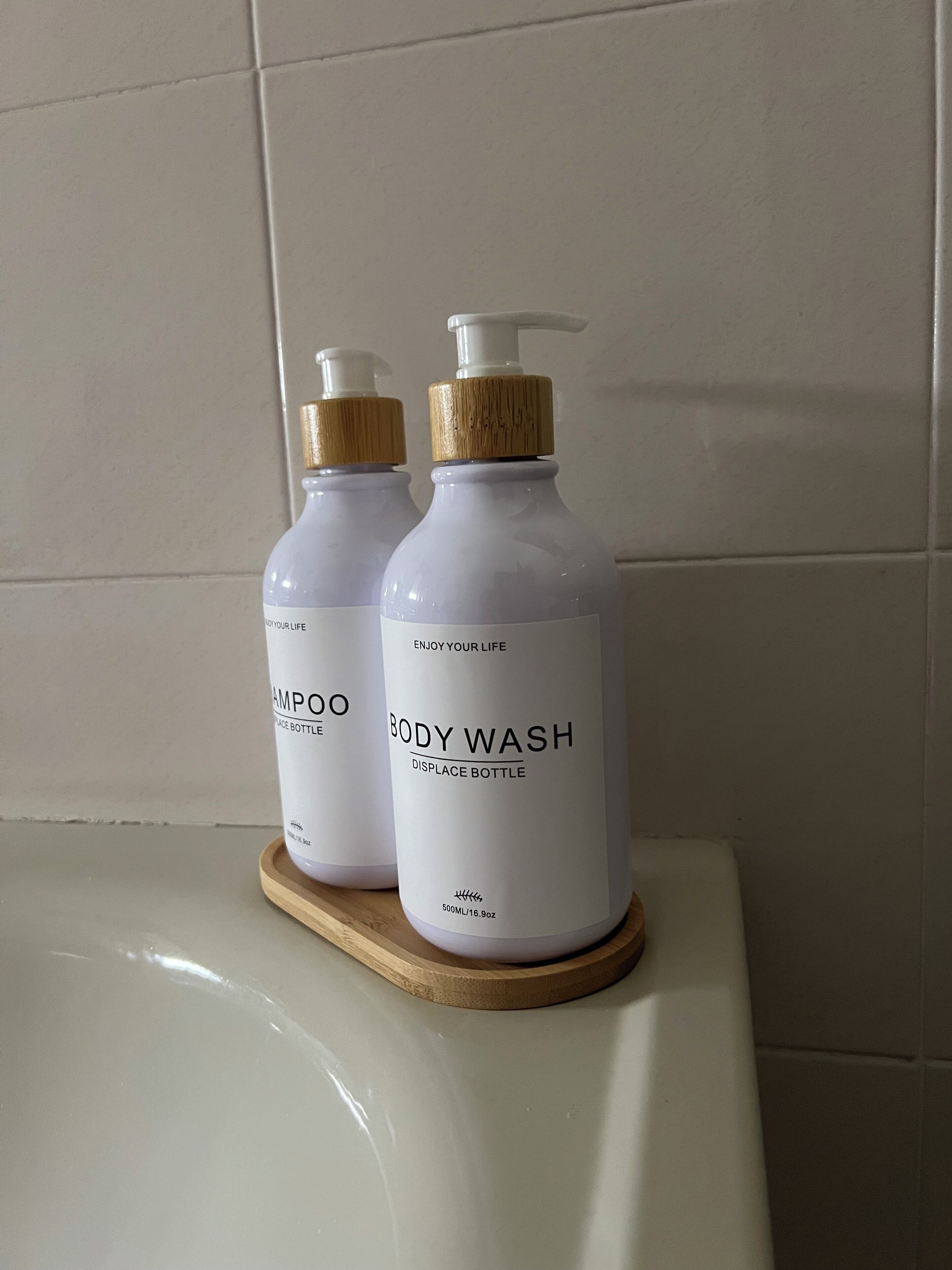 Deux bouteilles de gel douche sur un plateau en bois, posées sur le lavabo de la salle de bain.