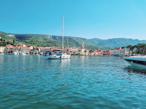 Ein Yachthafen mit Booten, eine Stadt mit roten Dächern und grüne Hügel im Hintergrund.