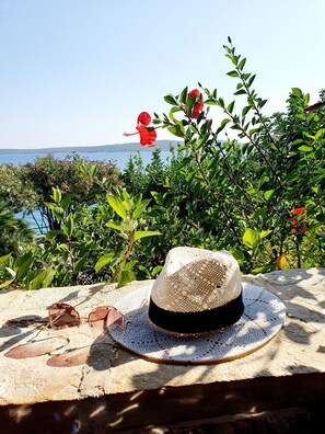 Un chapeau de paille posé sur une surface texturée, avec des lunettes de soleil et une fleur rouge en arrière-plan.