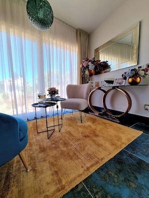 Ein modernes Wohnzimmer mit einer Couch, einem Couchtisch, einem Teppich, einem Spiegel und einem Fenster mit Vorhängen.