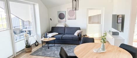 A modern living room with a sofa, coffee table, and chairs, a dining table with a vase, and a balcony with a railing.