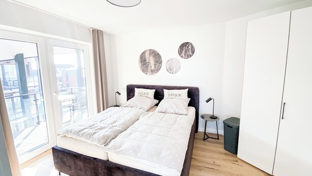 Une chambre à coucher moderne avec un lit, une armoire, une petite table et une poubelle.