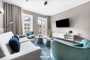 Ein modernes Wohnzimmer mit einer Couch, Sesseln, einem Couchtisch und einem an der Wand befestigten Fernseher.